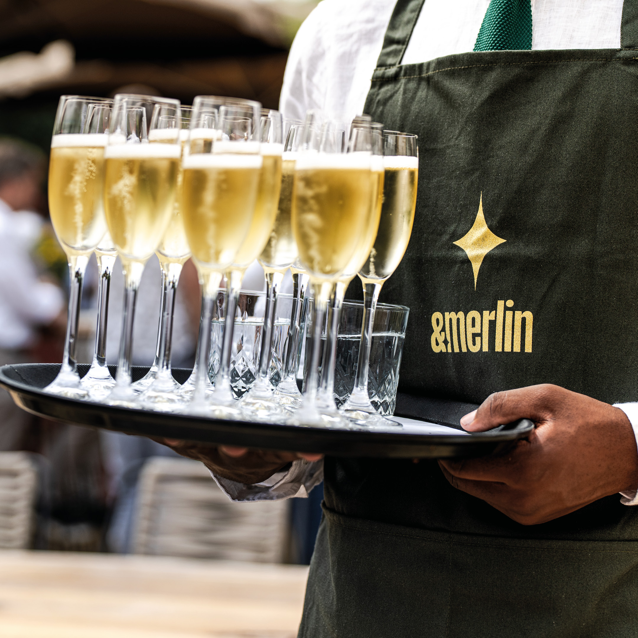 Waiter serving champagne glasses at an &merlin event