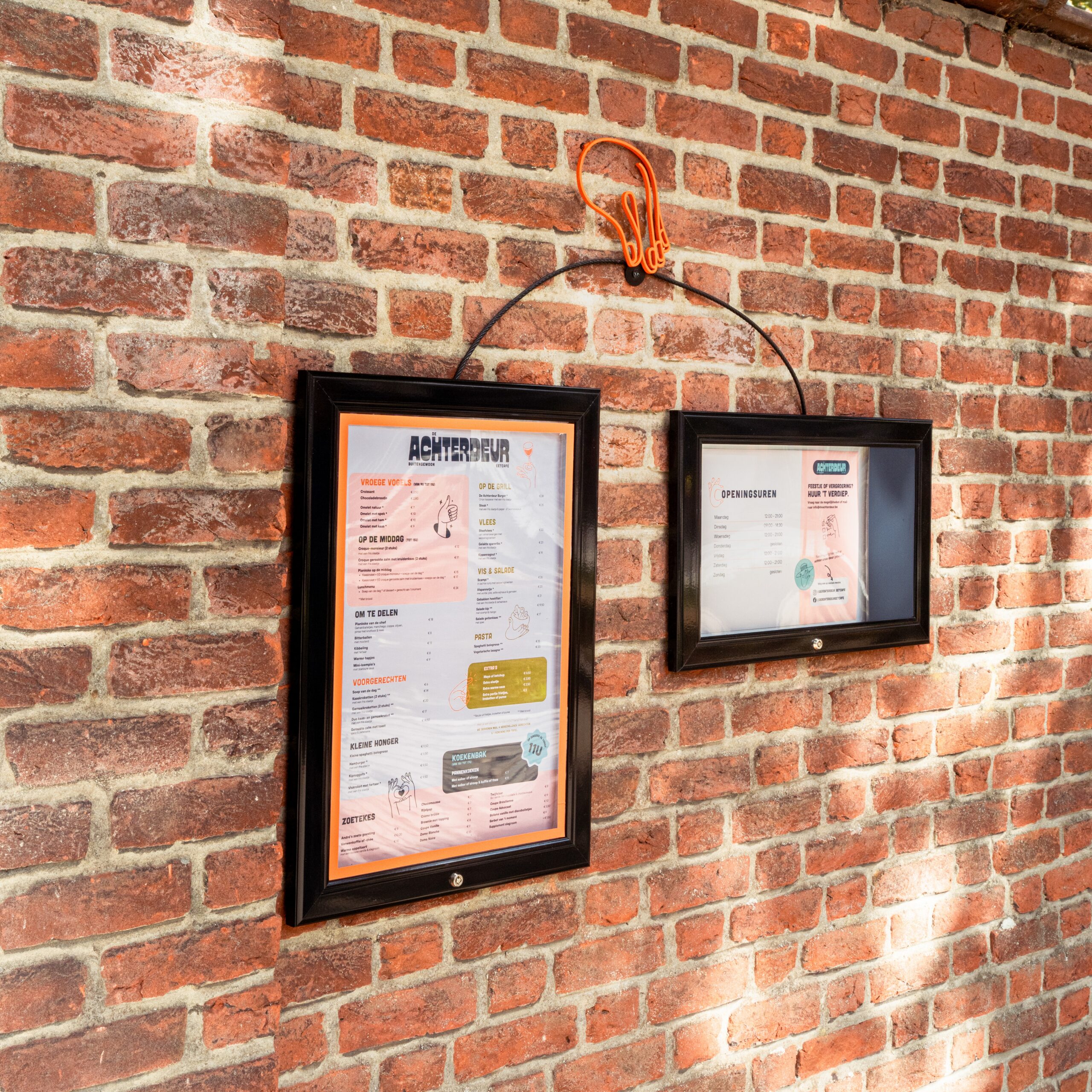Framed De Achterdeur menu boards on a brick wall