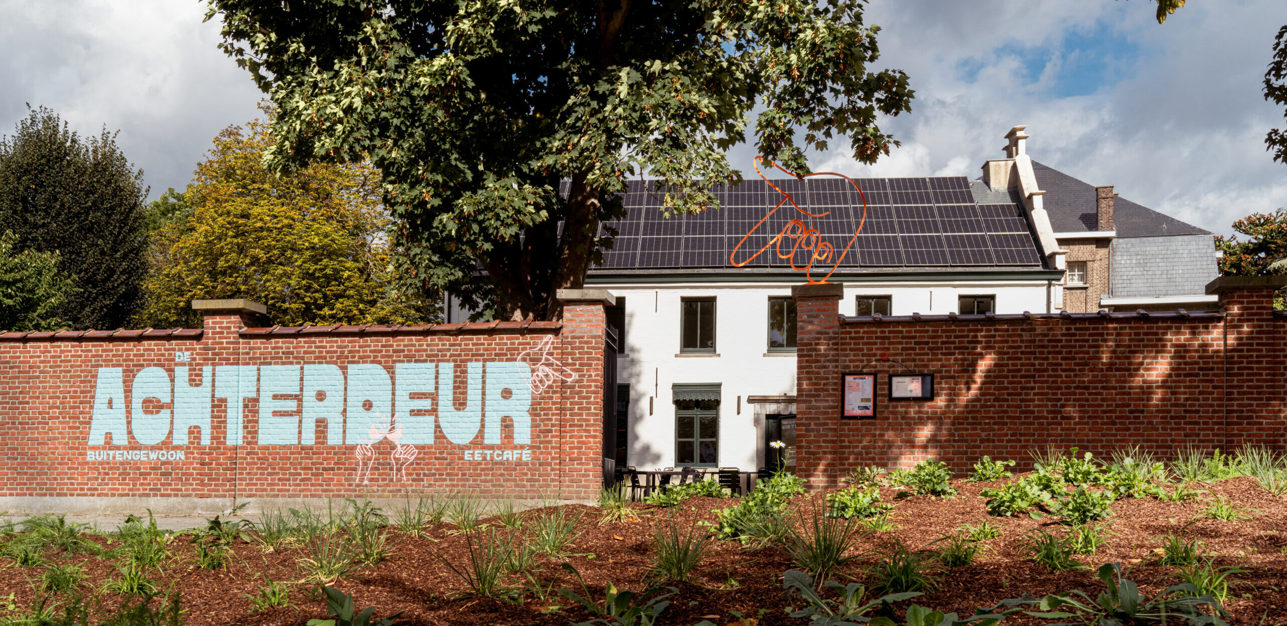 Painted De Achterdeur logo on the brick entrance wall in Niel, branding by Supermoon